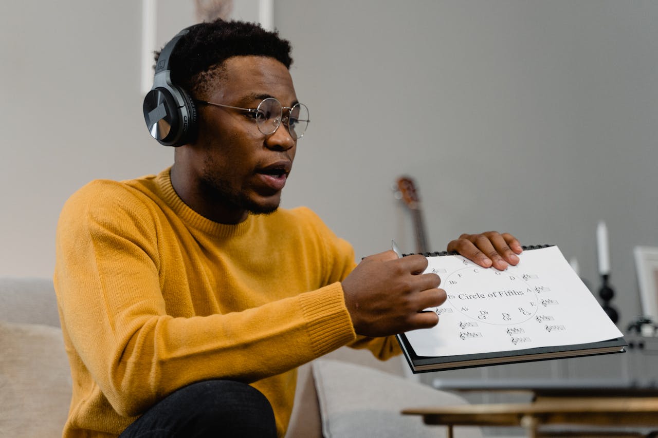African American man wearing headphones, teaching music theory with sheet. Indoor setting.